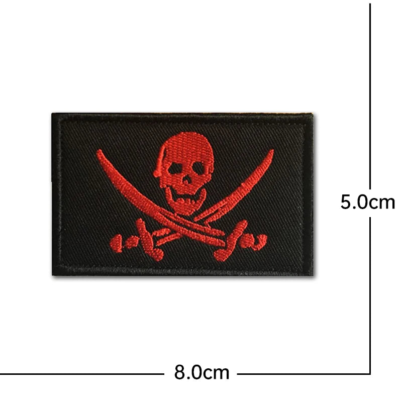 A black embroidery patch featuring a red pirate skull crossed with swords, measuring 5.0cm by 8.0cm.