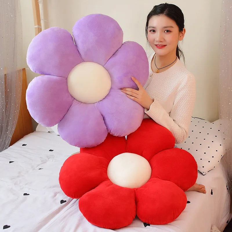 A woman is holding a large purple and red sunflower plush flower cushion on a white bed.