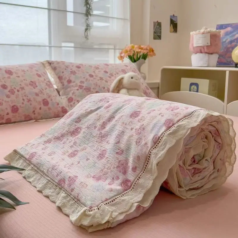 A pink quilt blanket with a floral print is rolled up on a pink surface.