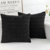 A set of two black knitted throw pillows with vertical ribbing resting on a white surface.