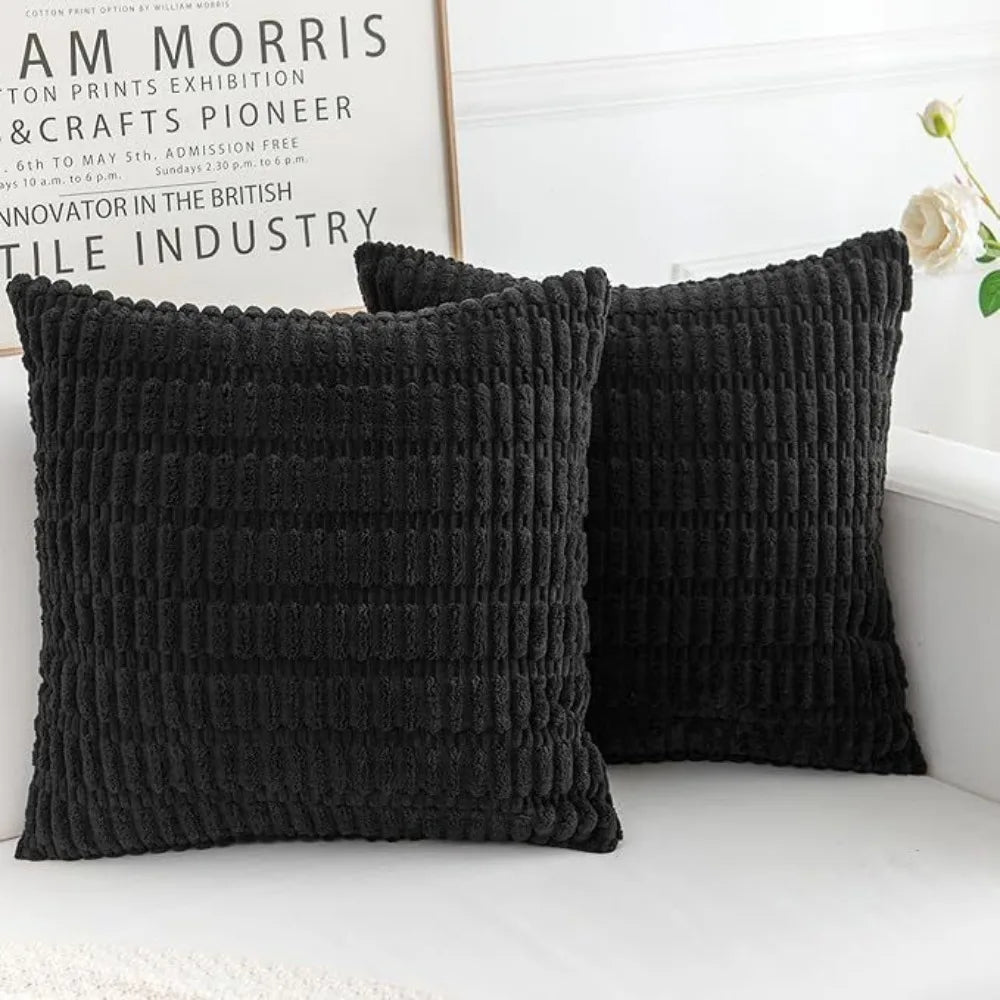 A set of two black knitted throw pillows with vertical ribbing resting on a white surface.