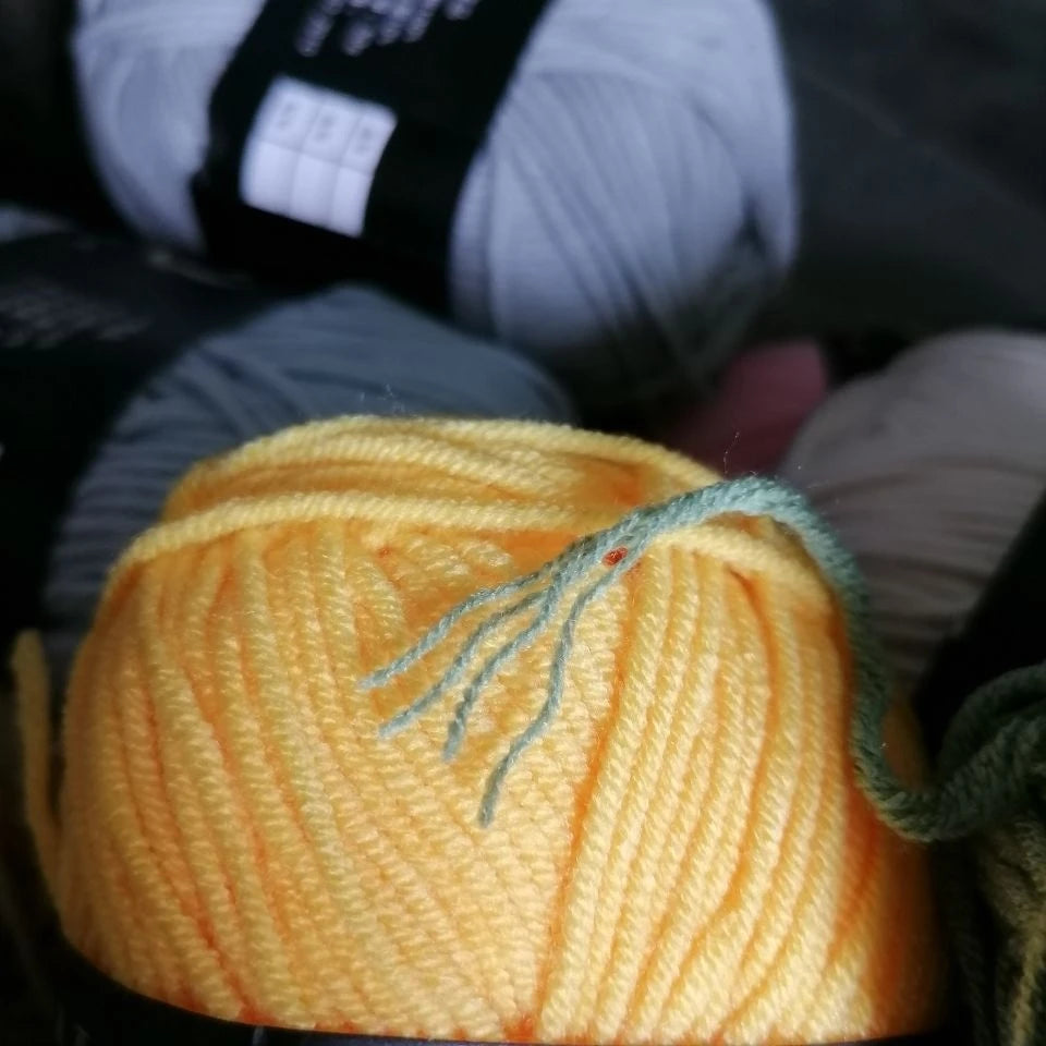 A ball of bright orange organic cotton 4ply knitting yarn with a green thread pulled out.
