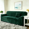 A deep emerald green stretch velvet sofa with a dark throw pillow sits in a bright living room.