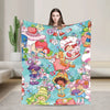 A woman holds up a colorful strawberry shortcake plush throw blanket featuring sweet fruit and character designs.