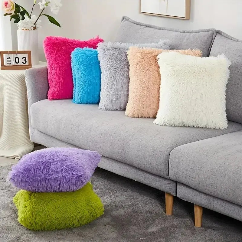 A collection of colorful velvet throw pillows in shades of pink, blue, gray, and cream displayed on a sofa.