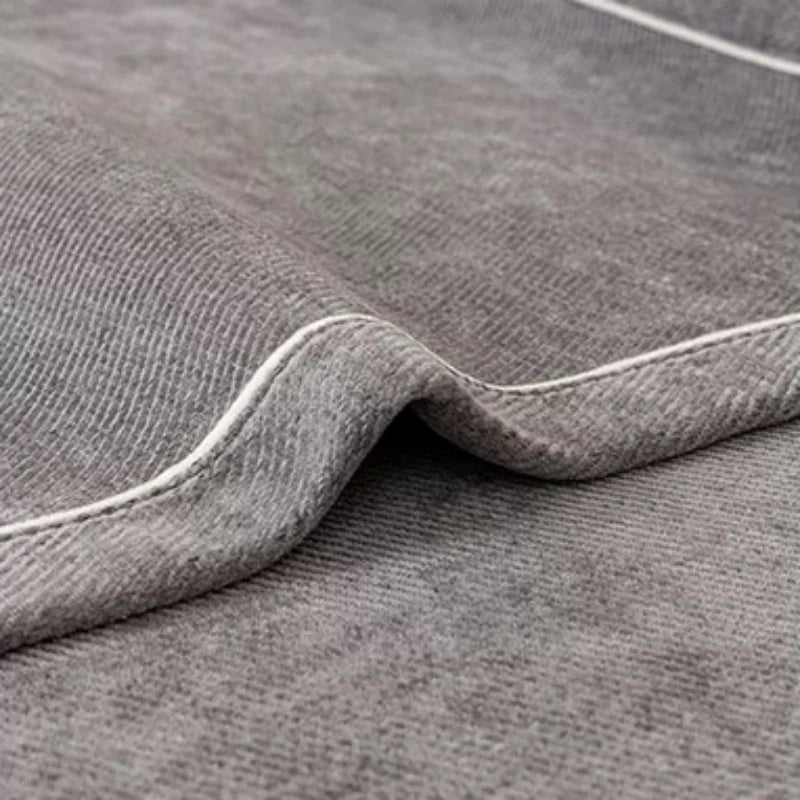 A close-up of a gray chenille sofa protector cover showing a folded edge and subtle texture.