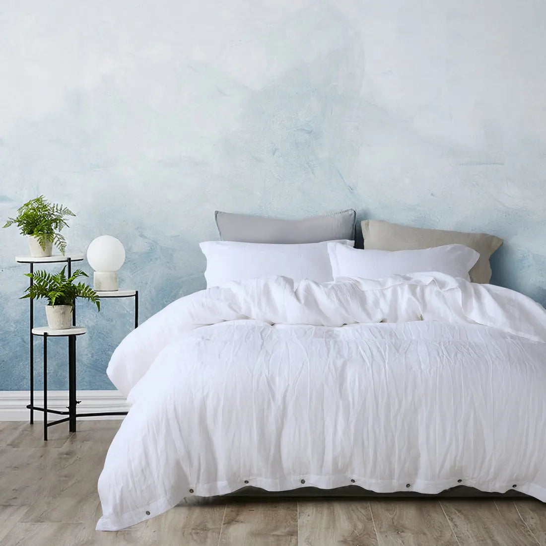A white luxury French linen duvet cover displayed on a bed against a light blue wall.