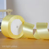 Roll of light yellow satin craft ribbon shown on a wooden surface.