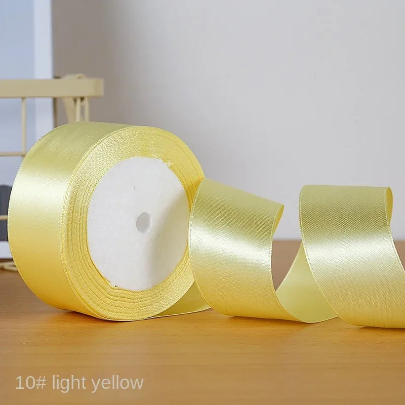 Roll of light yellow satin craft ribbon shown on a wooden surface.