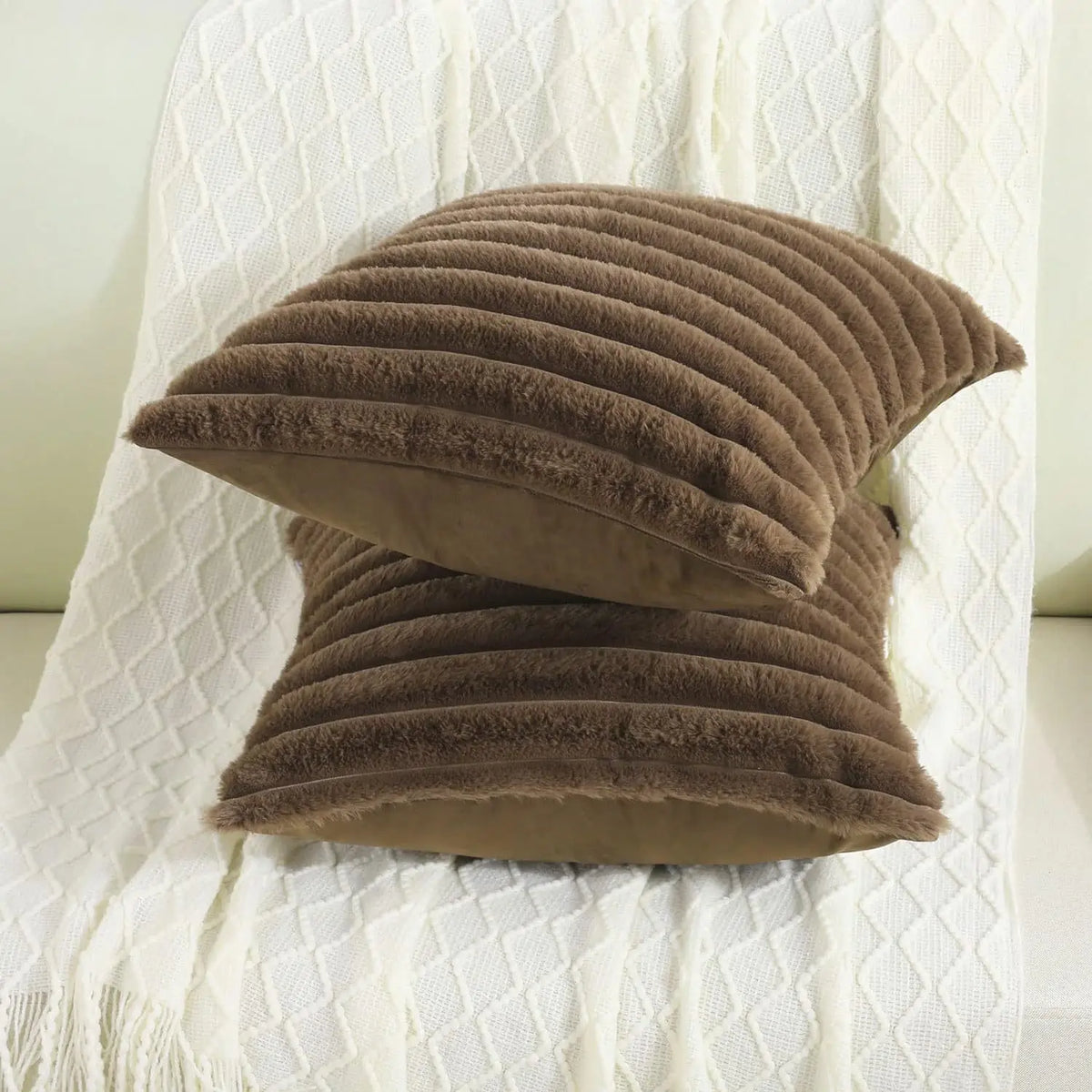 A stack of brown faux rabbit fur cushion covers resting on a white textured fabric.