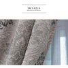 Close-up of gray European style sheer jacquard curtain panels with floral patterns hanging in a window.
