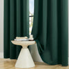 A solid dark green blackout window curtain hanging open, revealing a white pedestal with books and a glass.
