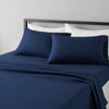 A navy blue microfiber flat fitted sheet set with white pillows on a bed.