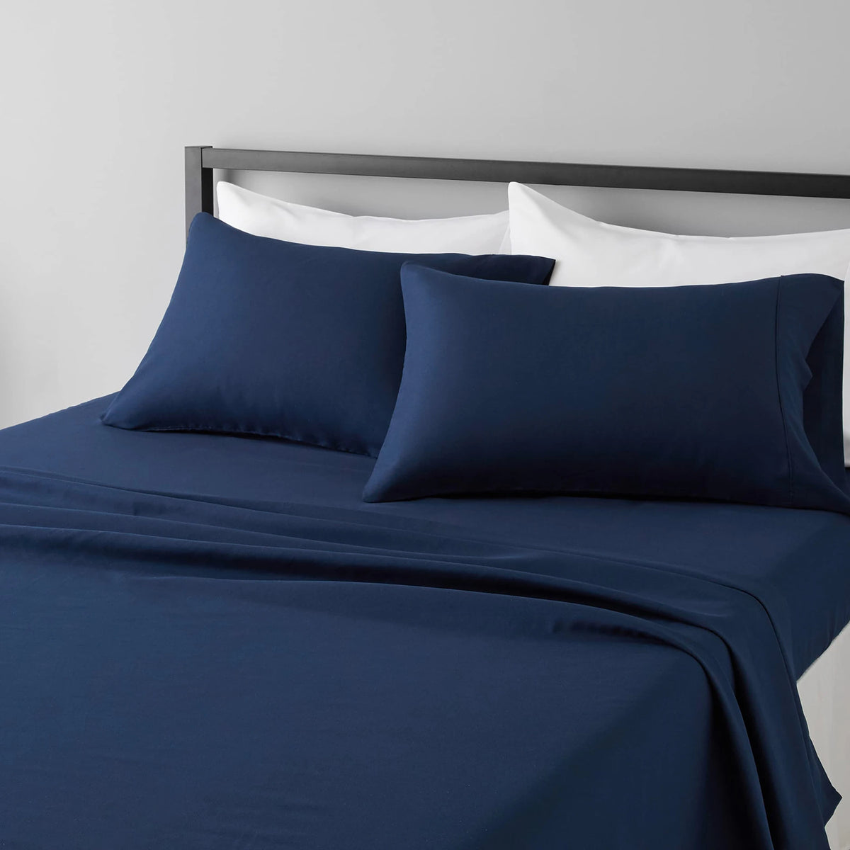 A navy blue microfiber flat fitted sheet set with white pillows on a bed.