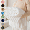 A person is holding a fluffy white striped flannel throw blanket, showcasing various shades of blue and gray options.