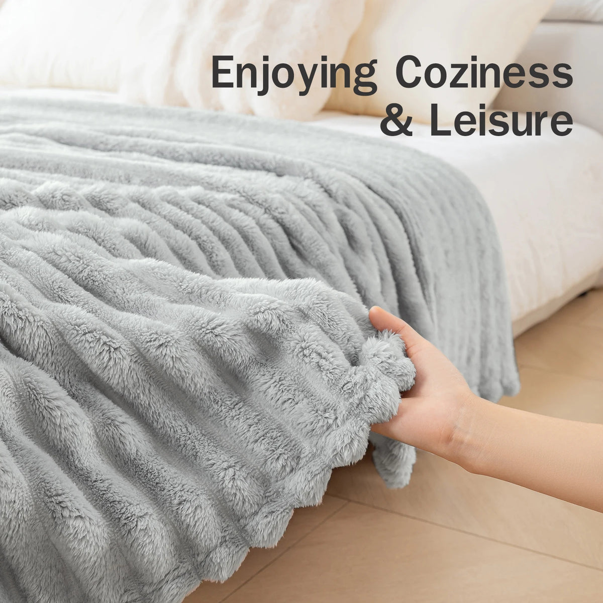 A hand is touching a soft gray flannel throw blanket draped over a bed, suggesting coziness and leisure.
