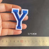 A hand holds a blue and white embroidered letter Y patch next to a ruler showing its dimensions.