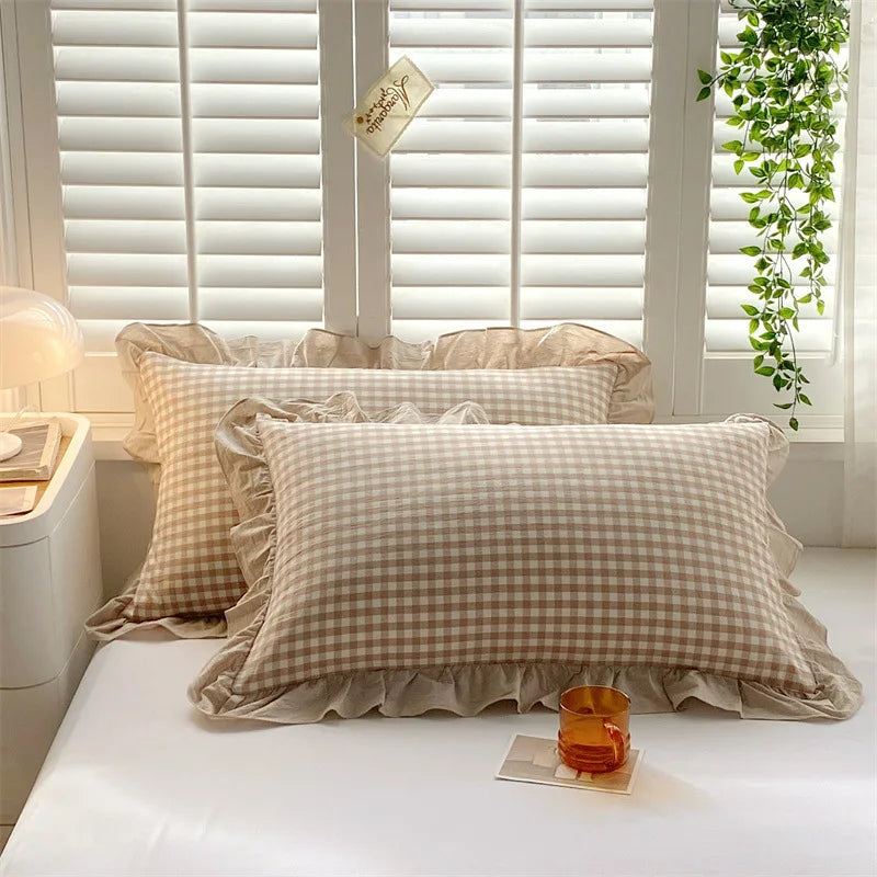 Two beige plaid cotton pillowcases with ruffled edges displayed on a white surface.