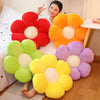 A plush sunflower flower cushion in various colors including red, orange, yellow, green, and purple is displayed on a wooden 