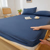 A dark blue fitted sheet is draped over a wooden bed frame, with a hand touching the fabric.