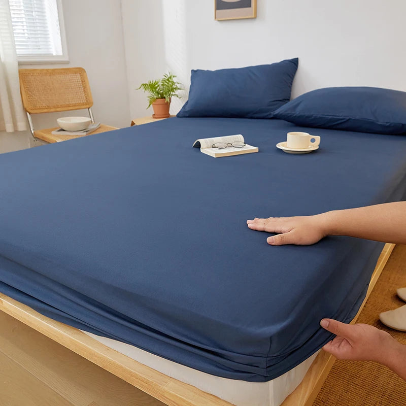 A dark blue fitted sheet is draped over a wooden bed frame, with a hand touching the fabric.