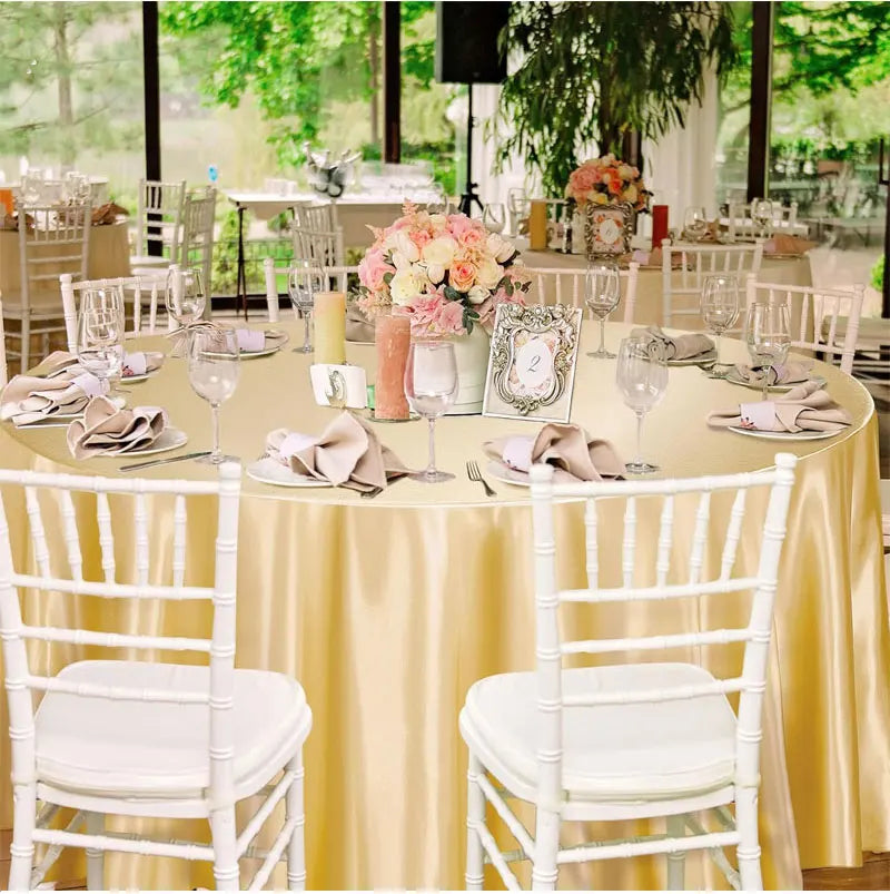Elegant satin round tablecloths set for an event featuring white chairs and floral centerpieces.