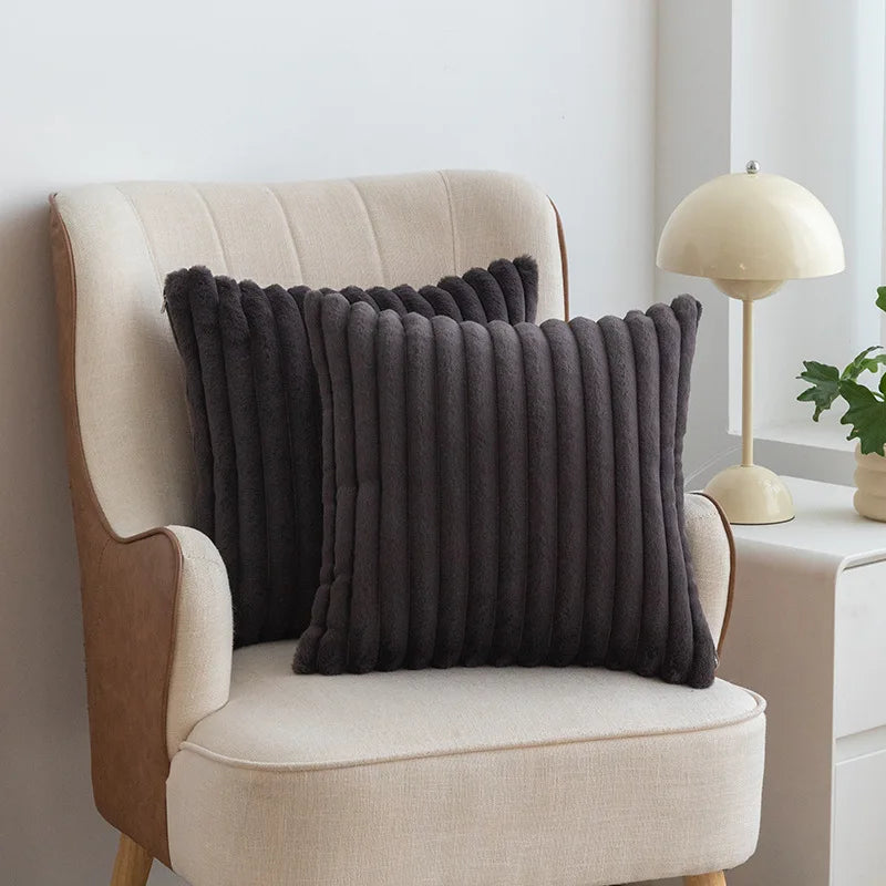 A dark gray faux fur striped decorative throw pillow cover resting on a cream upholstered armchair.