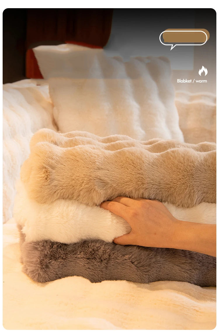A hand is touching a fluffy, light beige faux fur blanket on a white bed, with a dark gray blanket underneath.