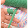 A hand is shown manipulating thick green polyester blended yarn, demonstrating its texture and use for crafting.