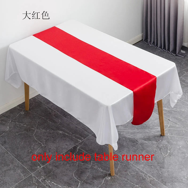 White tablecloth with a red satin table runner displayed on a wooden table.