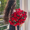 A vibrant bouquet of red roses and green filler flowers held by a person, with a knitted throw blanket visible.