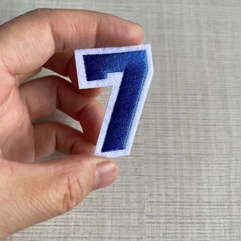 A hand holds a white and navy blue embroidered number 7 patch for apparel.
