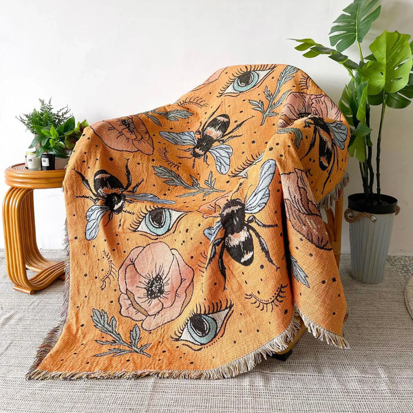 A bohemian geometric throw blanket featuring an orange background with stylized bees and eyes.