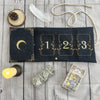 A black pouch for storing tarot cards featuring a crescent moon and gold accents, next to a feather and a candle.