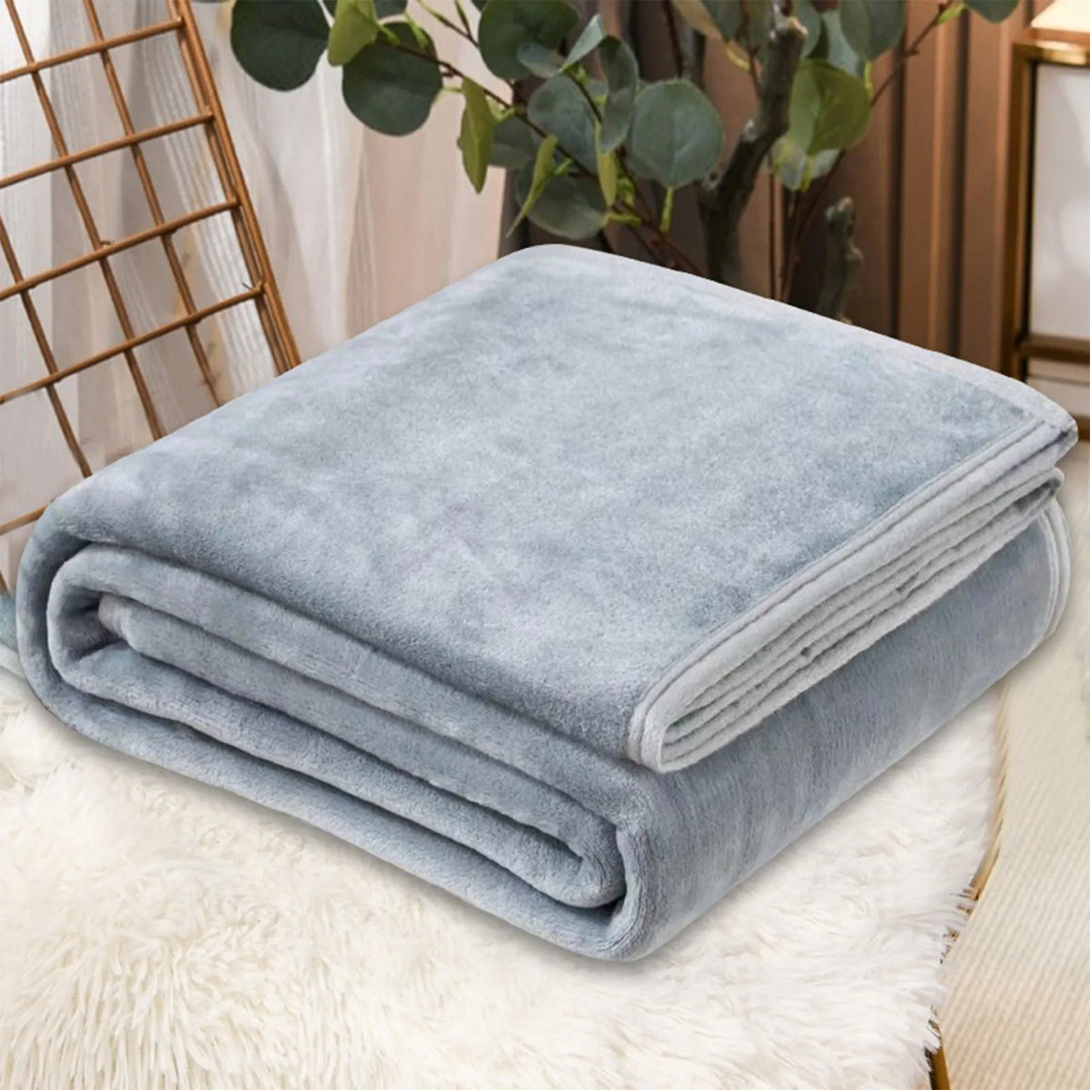 A folded light blue cozy coral fleece throw blanket resting on a white fluffy rug.