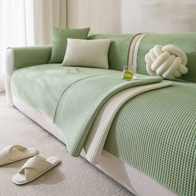 A light green machine washable anti-slip sofa slipcover with cream accents and a white knitted decorative pillow.
