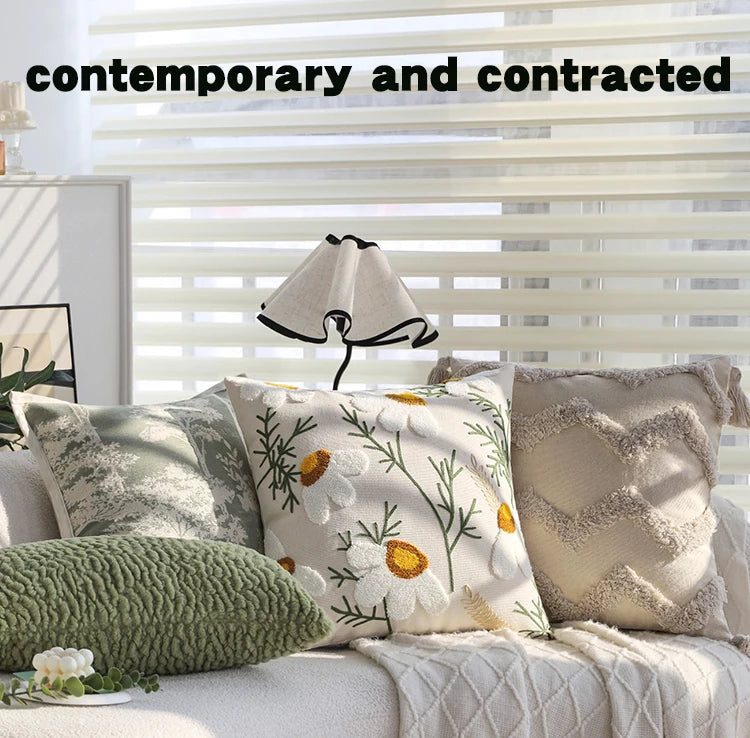 A close-up of a beige embroidered floral cushion cover resting on a light-colored sofa with white blinds.