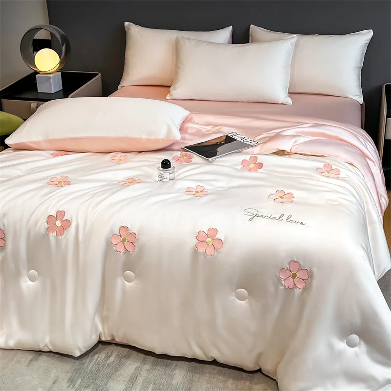 A white and pink embroidered quilt with floral designs is displayed on a bed.