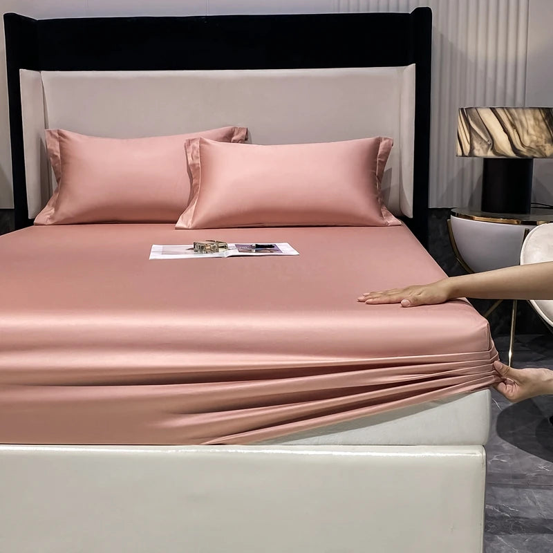 A pink luxury fitted sheet and pillow set displayed on a bed with a black headboard.