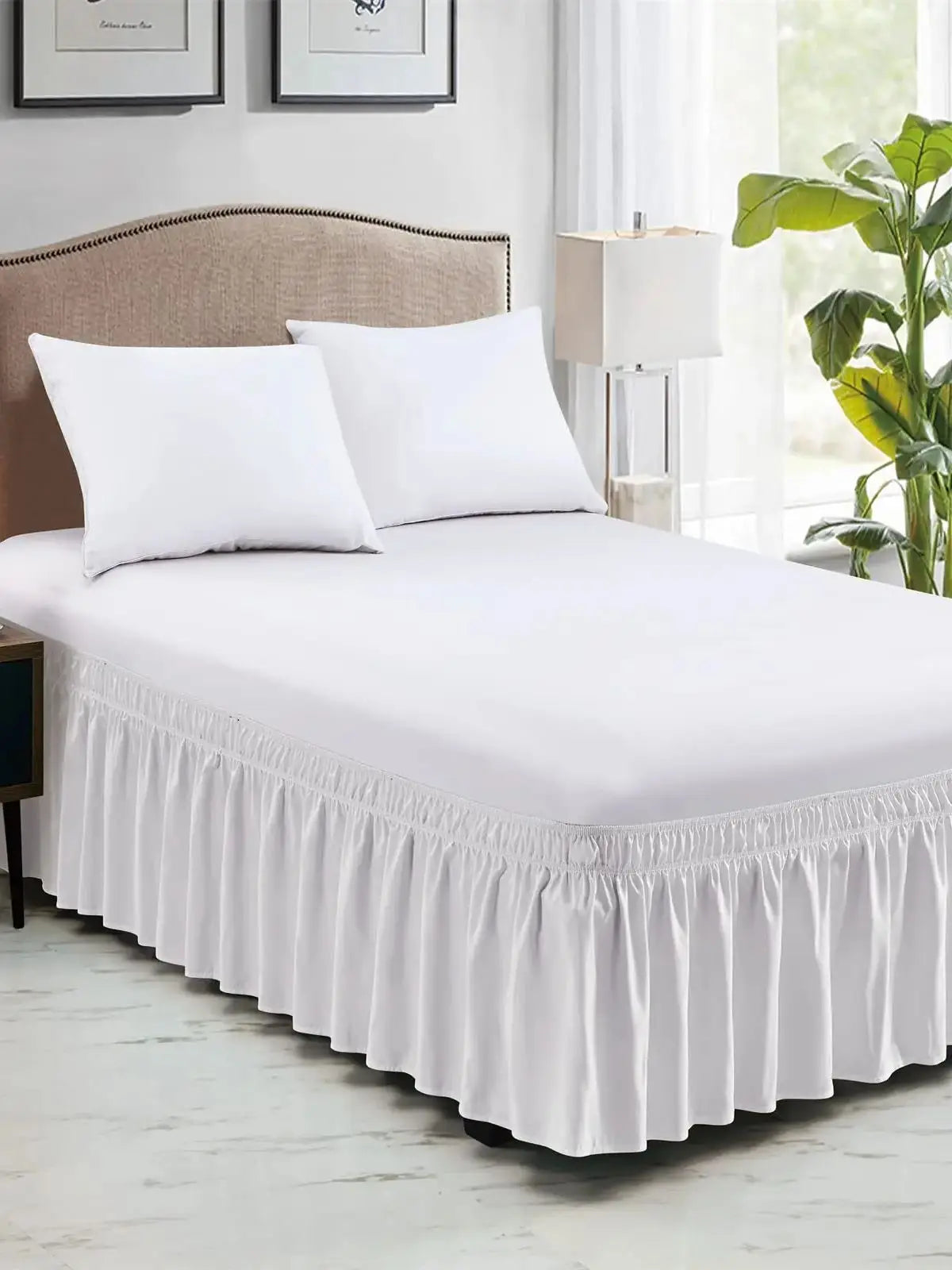 White wrap around elastic bed skirt with white pillows on a bed.