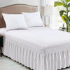 White elegant elastic bed skirt with ruffles and white pillows on a bed.