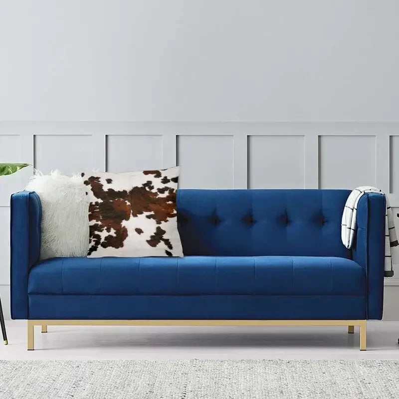 A deep blue velvet sofa adorned with a white faux fur and brown cowhide print cushion covers.