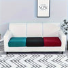 A white sofa with three colored cushions (teal, black, and red) on a patterned rug.