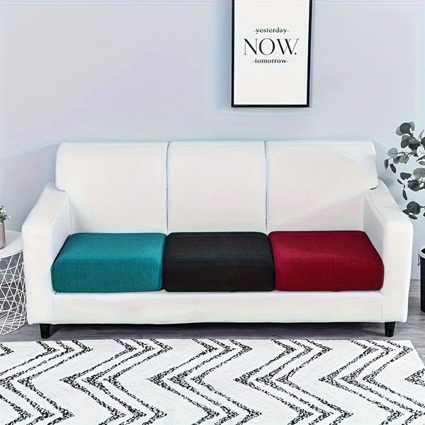 A white sofa with three colored cushions (teal, black, and red) on a patterned rug.