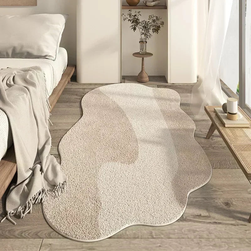 A beige irregular plush area rug is placed on a light wood floor in a bright room.