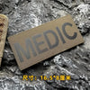 A dark olive green tactical hook and loop patch labeled MEDIC resting on a rough gray rock surface.