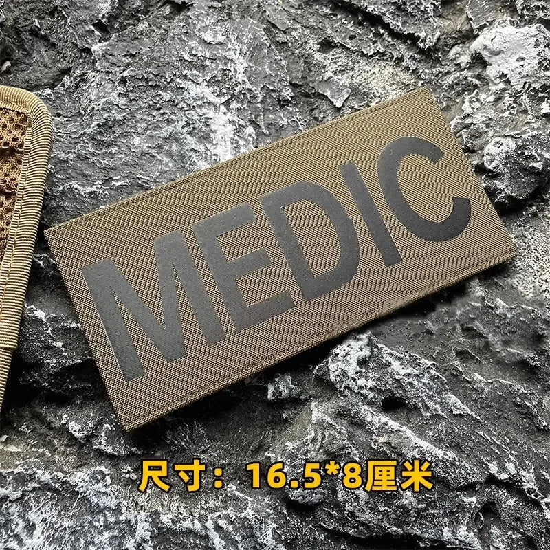 A dark olive green tactical hook and loop patch labeled MEDIC resting on a rough gray rock surface.