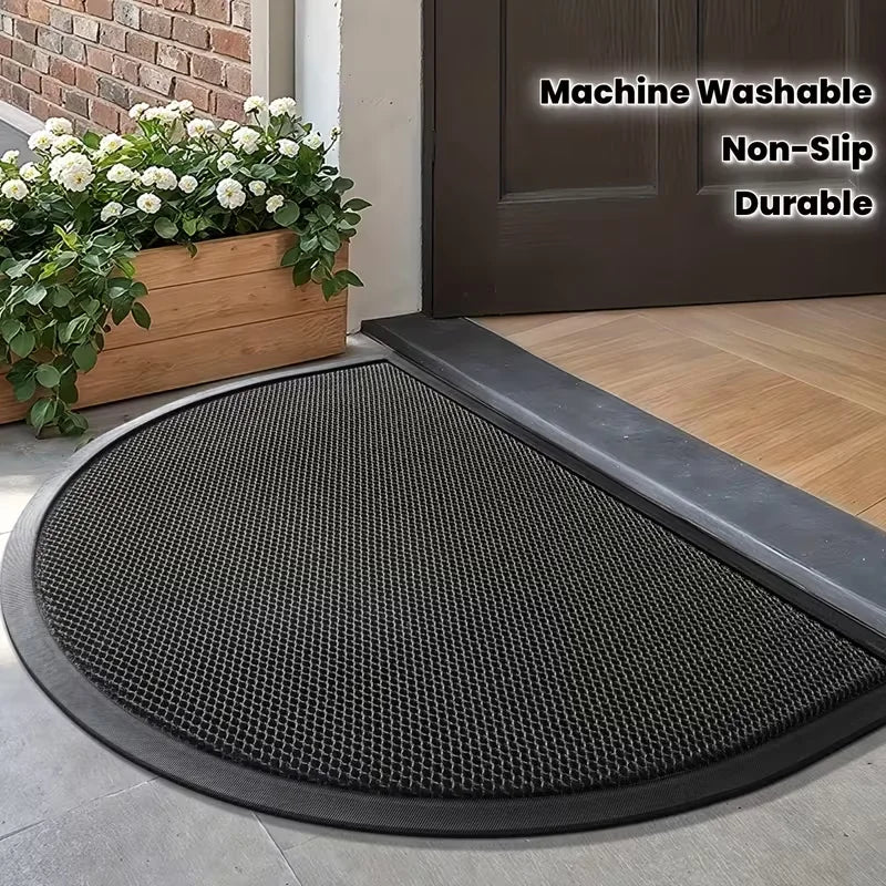 A black half-round non-slip PVC door mat placed on a wooden floor near a dark brown door.