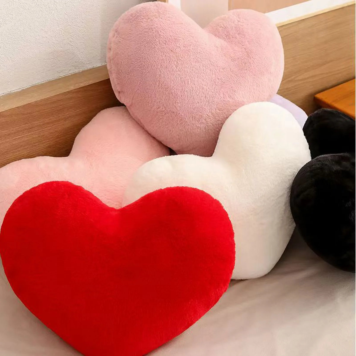 A collection of heart-shaped throw pillows in pink, white, and red velvet textures.