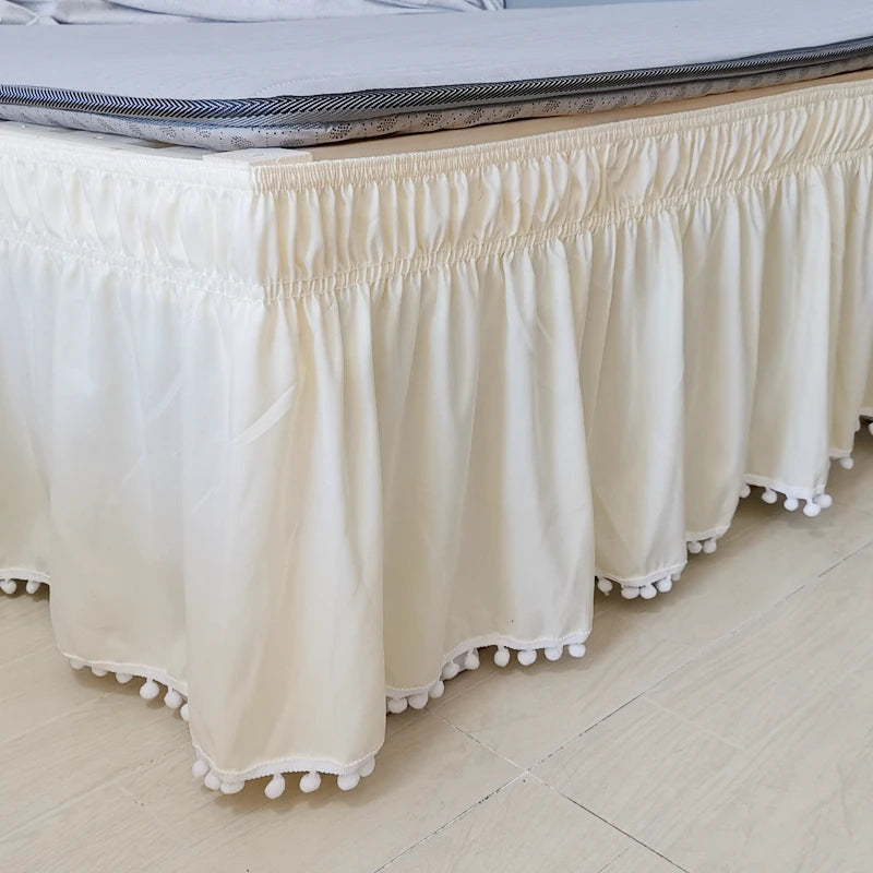 A cream-colored elegant elastic bed skirt with gathered fabric and decorative fringe